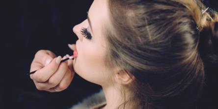 Woman sitting on a chair having her makeup done. She is facing away from the camera to the left.