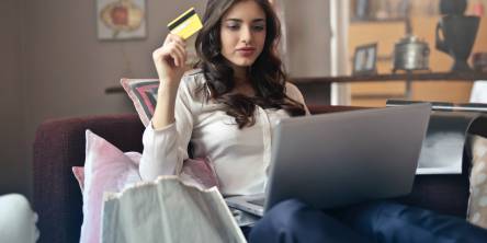 Woman sitting on a couch looking at a laptop with a credit card in her right hand.