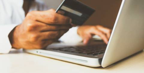 A man looking a credit card and putting the details into a laptop.