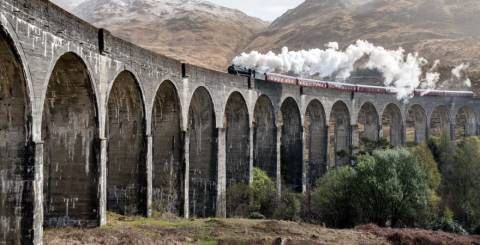 A side view of the Glenfinnan Viaduct in Scotland with a train passing over the top.