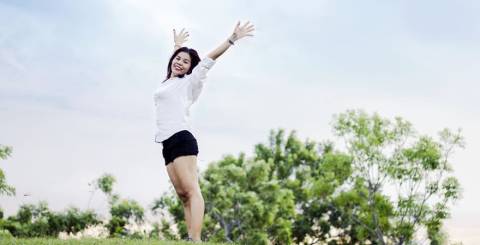 Woman on hill looking happy and content with the sky behind her. Her arms are stretched upward to the sky with a smile.