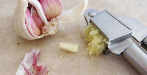 Fresh Garlic Cloves and Crushed Garlic in a Press Fresh garlic cloves with skin and a garlic press crushing garlic on a kitchen counter.