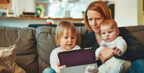 two babies and woman sitting on sofa while holding baby and watching on tablet